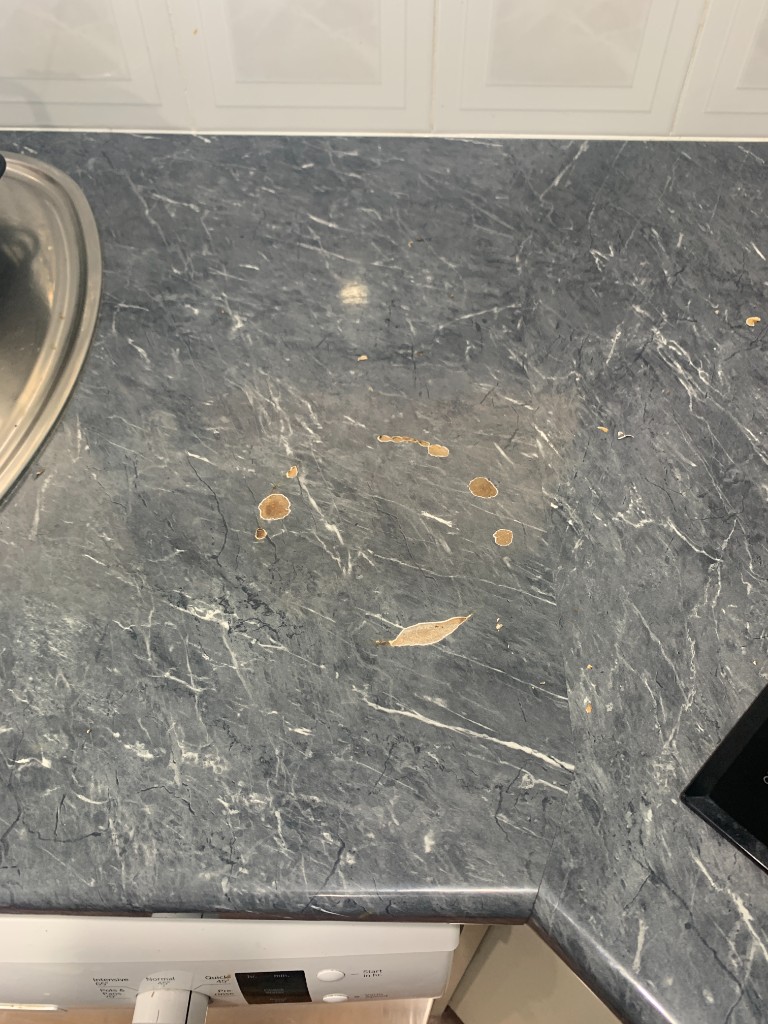 Stone- or laminate-look kitchen benchtop with localised chip and burn damage before repair