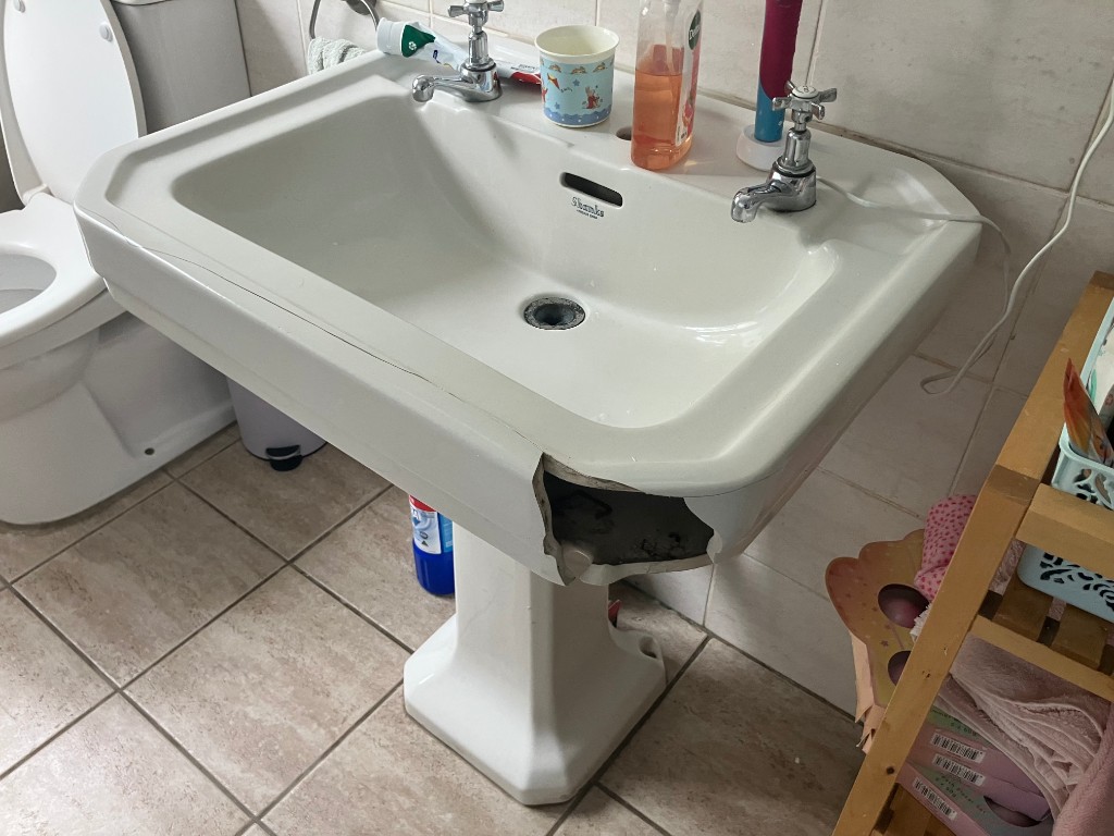 White ceramic pedestal bathroom sink with impact damage and a long crack before repair