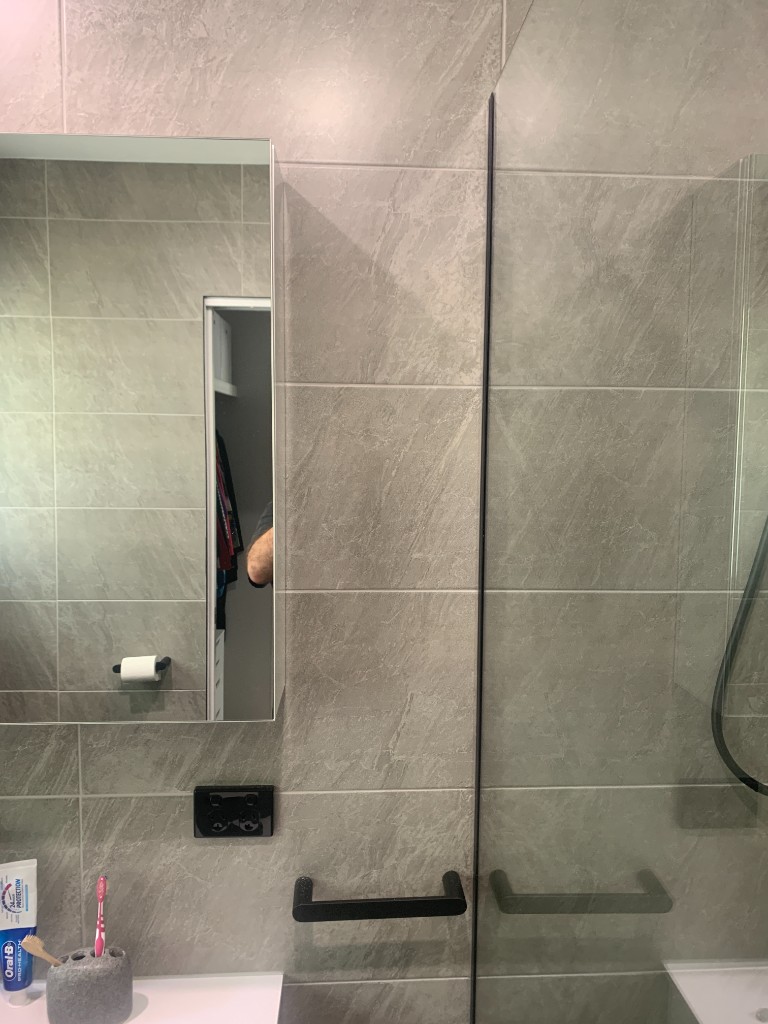 Same bathroom tiled wall after repair—mirror, black fittings and shower screen
