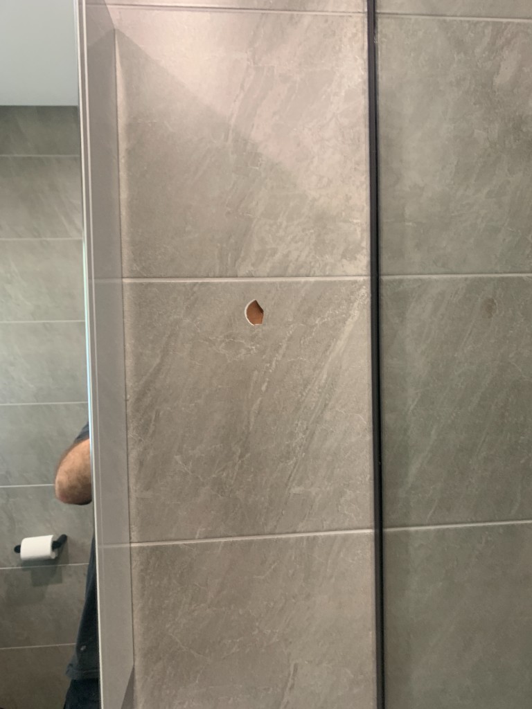 Grey marble-look wall tile with chip exposing terracotta body before repair